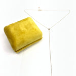 Gold necklace on a white background with a yellow fabric square