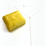Gold necklace on a white background with a yellow fabric square