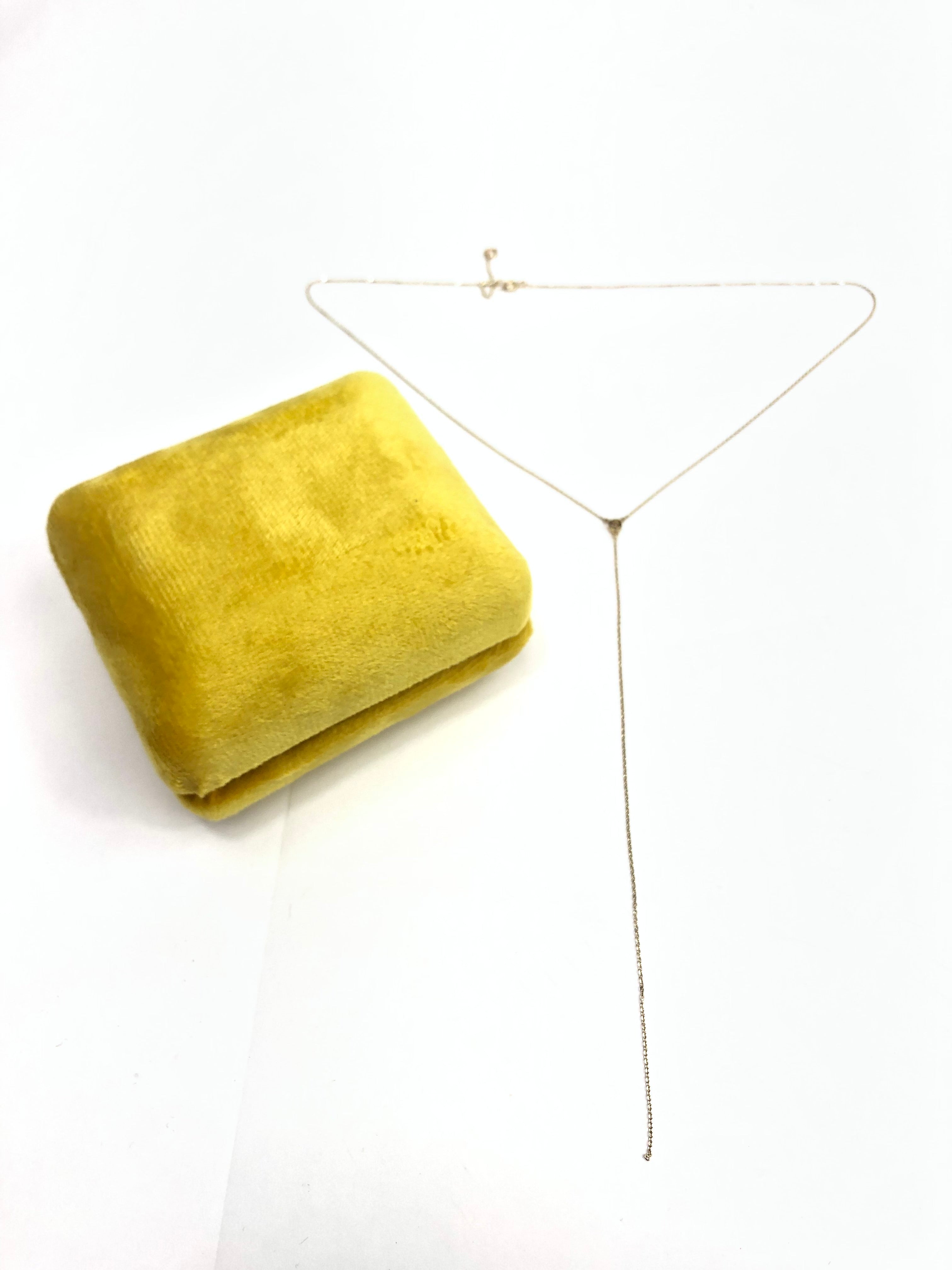 Gold necklace on a white background with a yellow fabric square
