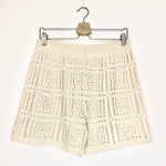 Beige crochet shorts on a hanger against a white background