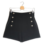 Black shorts with silver buttons on a hanger against a white background