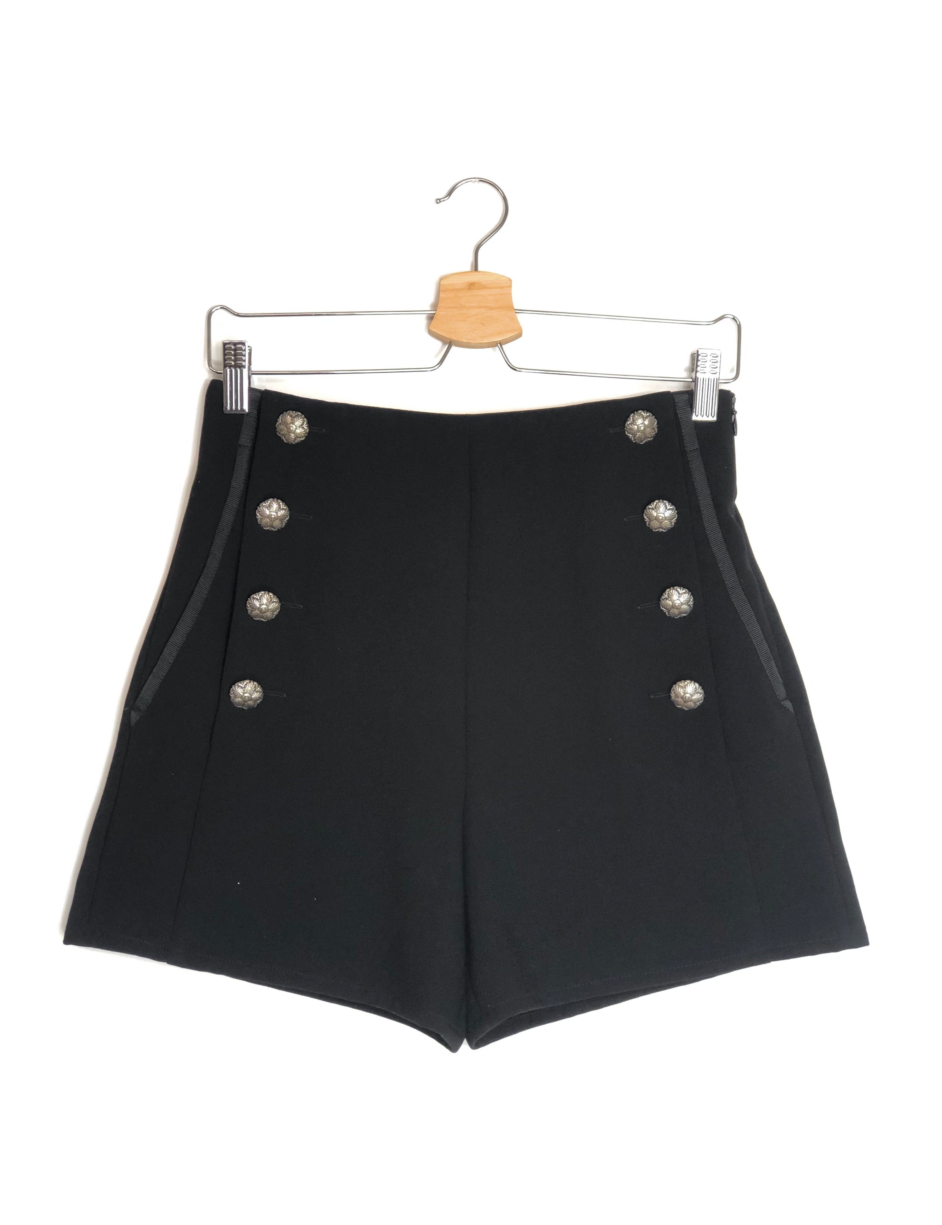Black shorts with silver buttons on a hanger against a white background