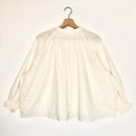 White lace blouse on a wooden hanger against a white background