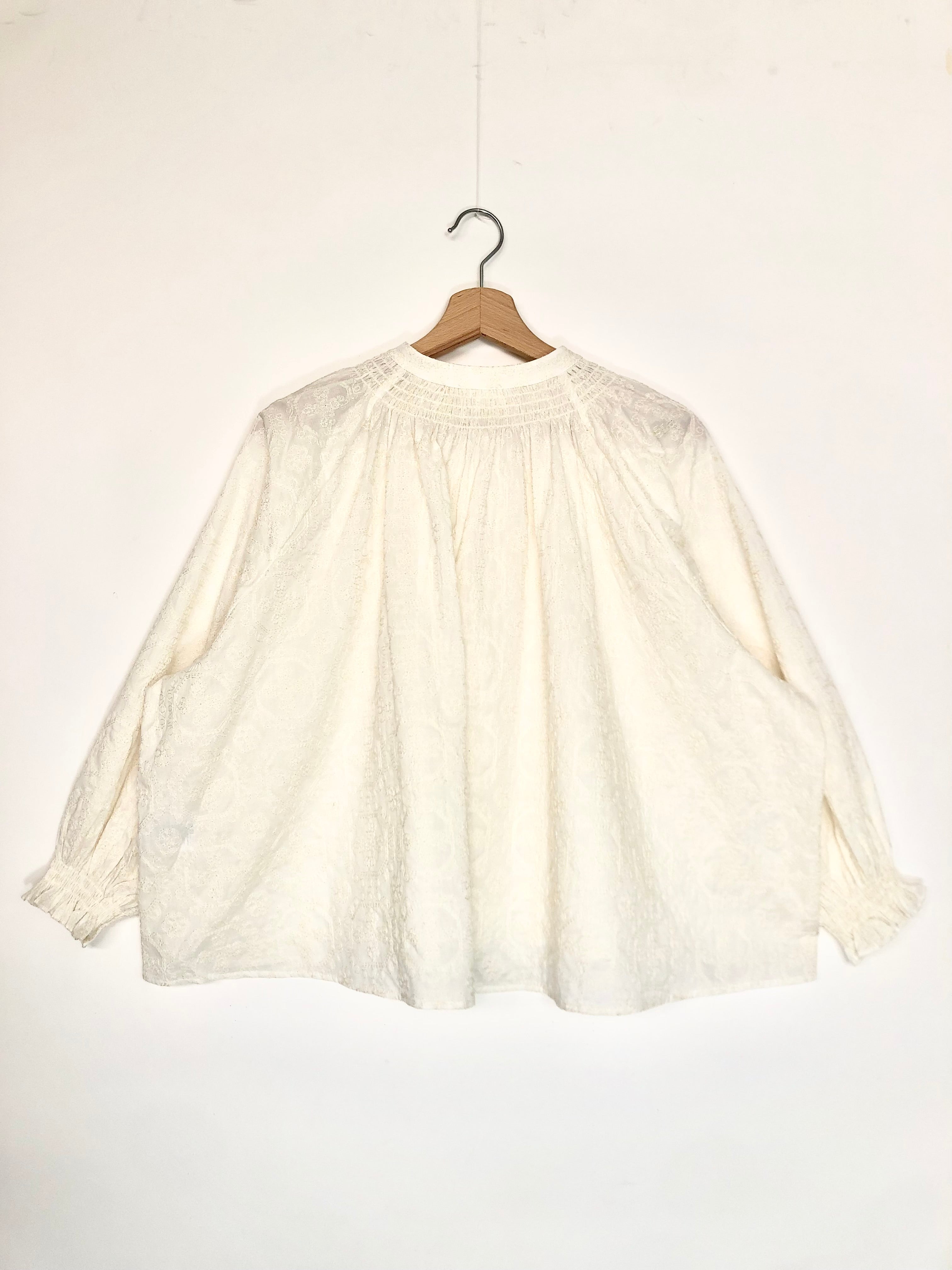 White lace blouse on a wooden hanger against a white background