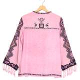 Pink poncho with patterned sleeves and fringes on a hanger against a white background