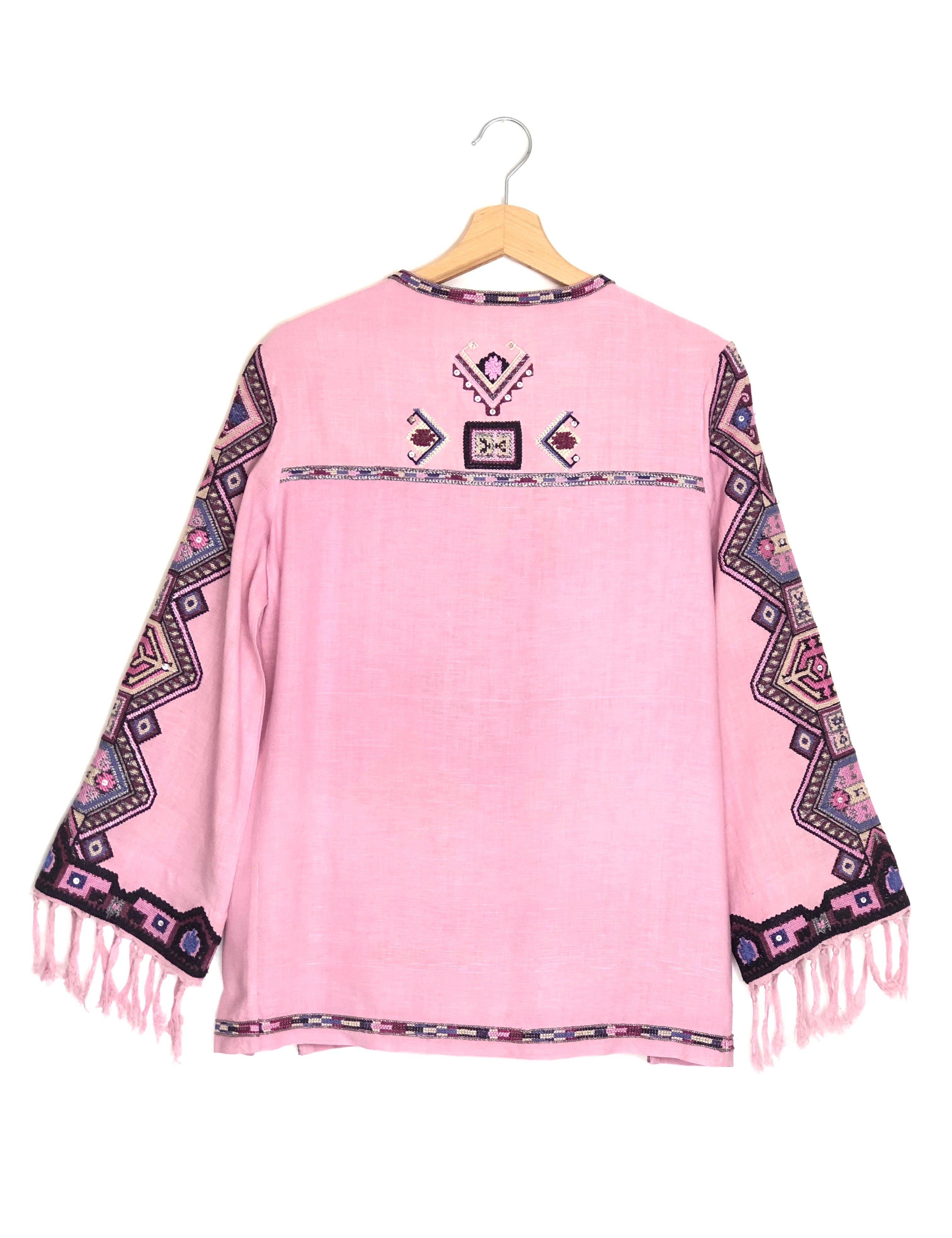 Pink poncho with patterned sleeves and fringes on a hanger against a white background