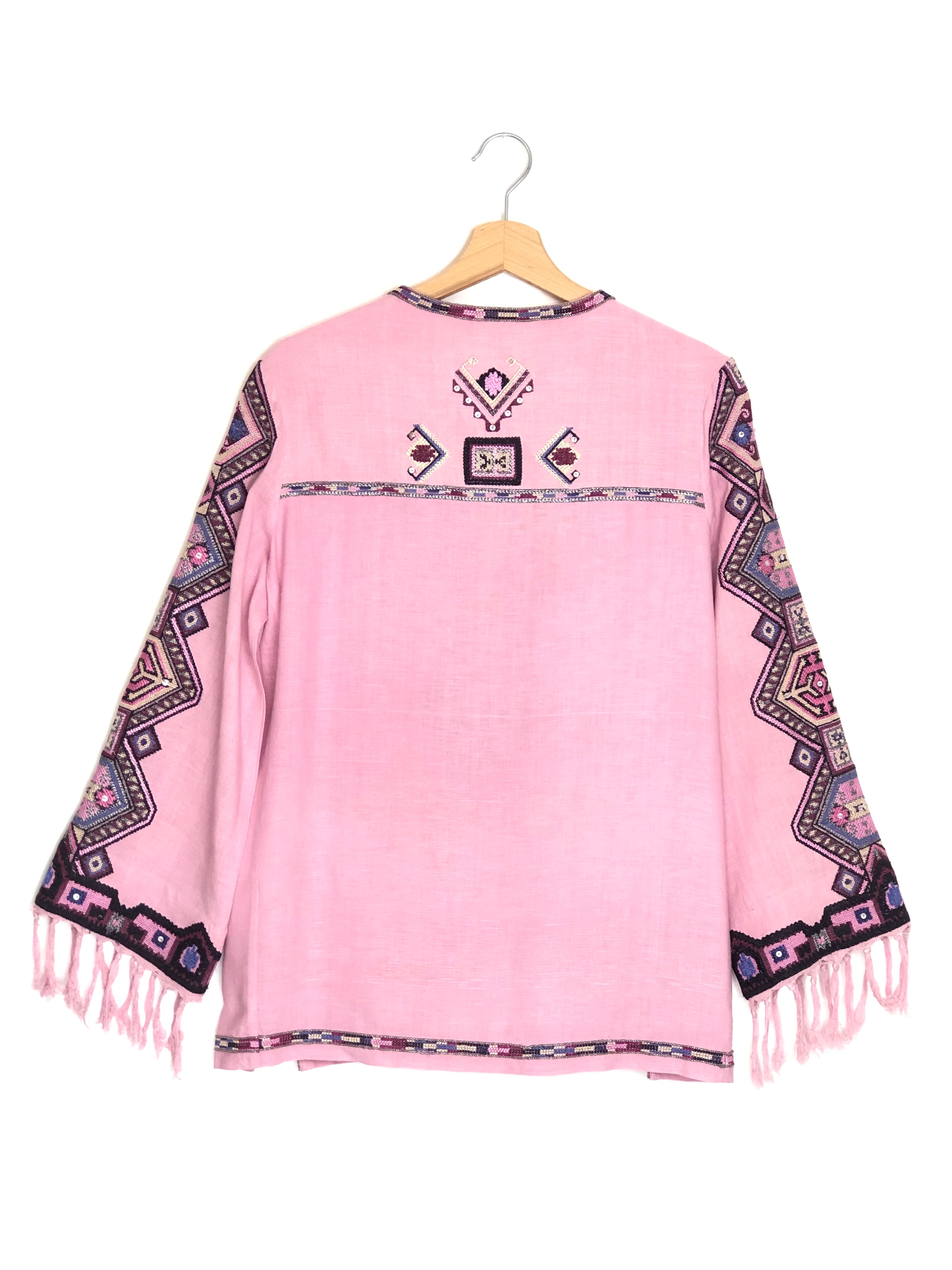 Pink poncho with patterned sleeves and fringes on a hanger against a white background
