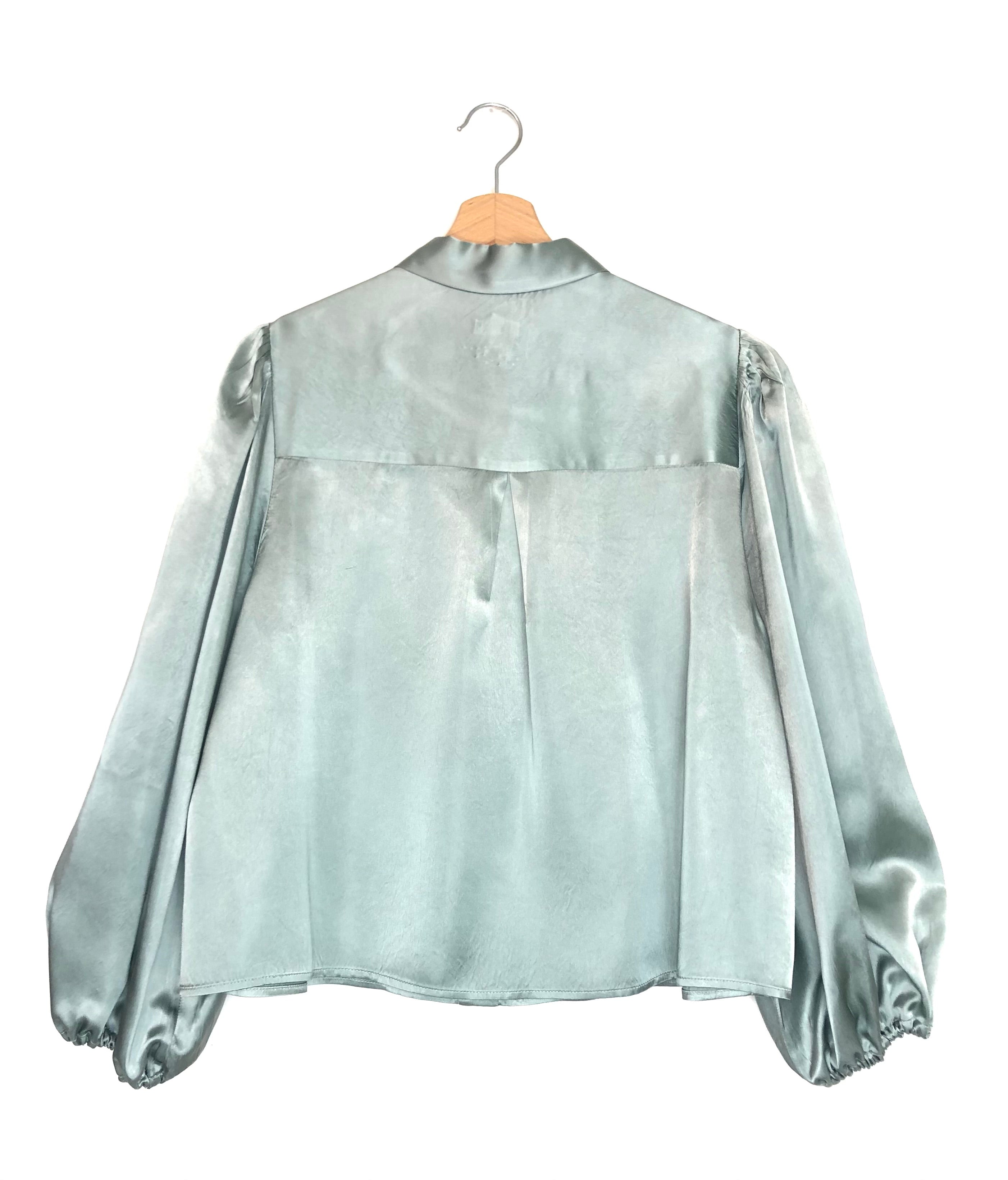 Rain-blue blouse on a hanger against a white background