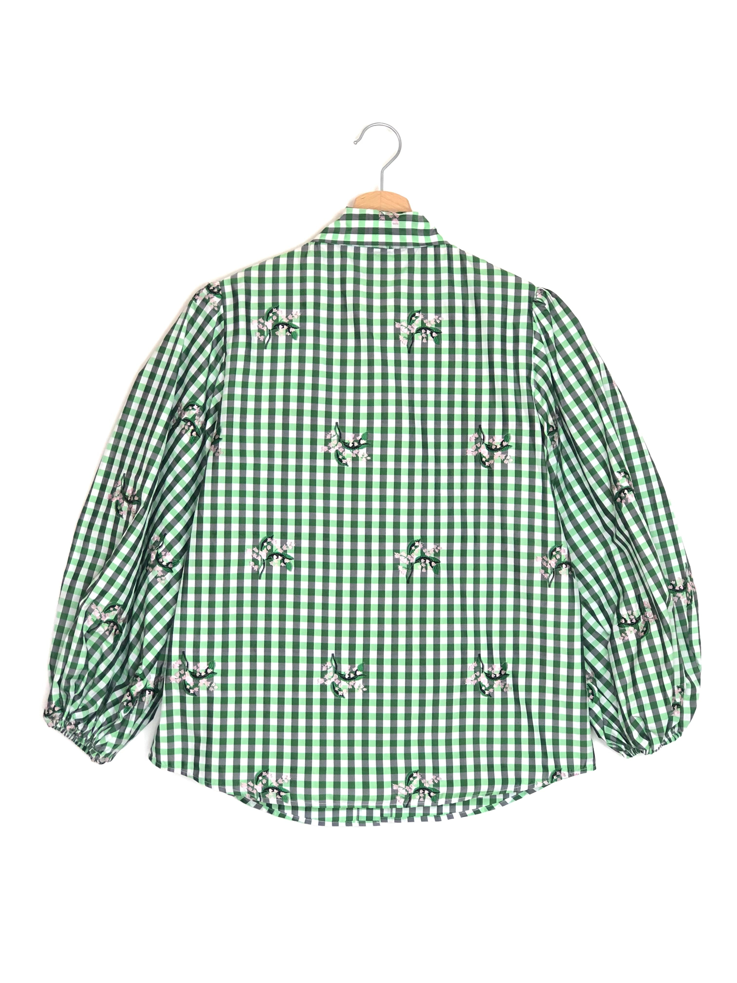 Green checkered shirt with embroidered details on a hanger against a white background
